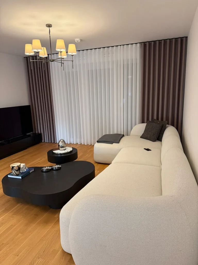 Weiße Gardinen und taupefarbene Vorhänge im Wohnzimmer mit hellem Sofa und schwarzen Couchtischen