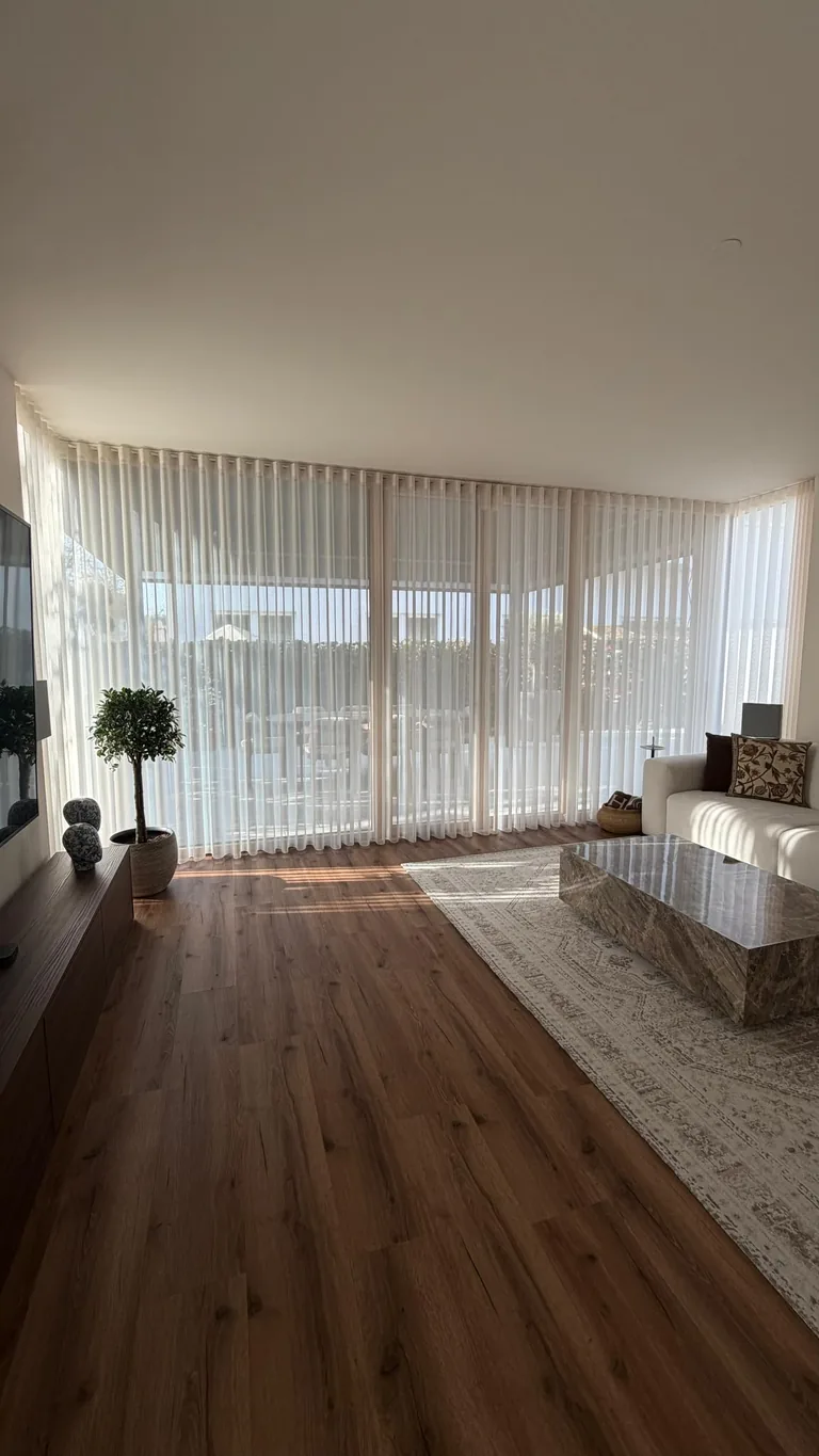 Weiße Gardinen an der Fensterfront im Wohnbereich mit beigem Sofa und hellem Couchtisch