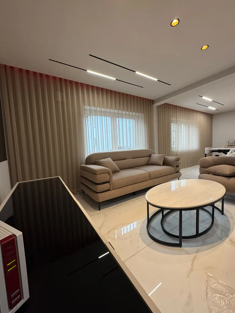 Beige transparente Wellengardinen an zwei Fenstern im Wohnzimmer mit hellem Marmorboden