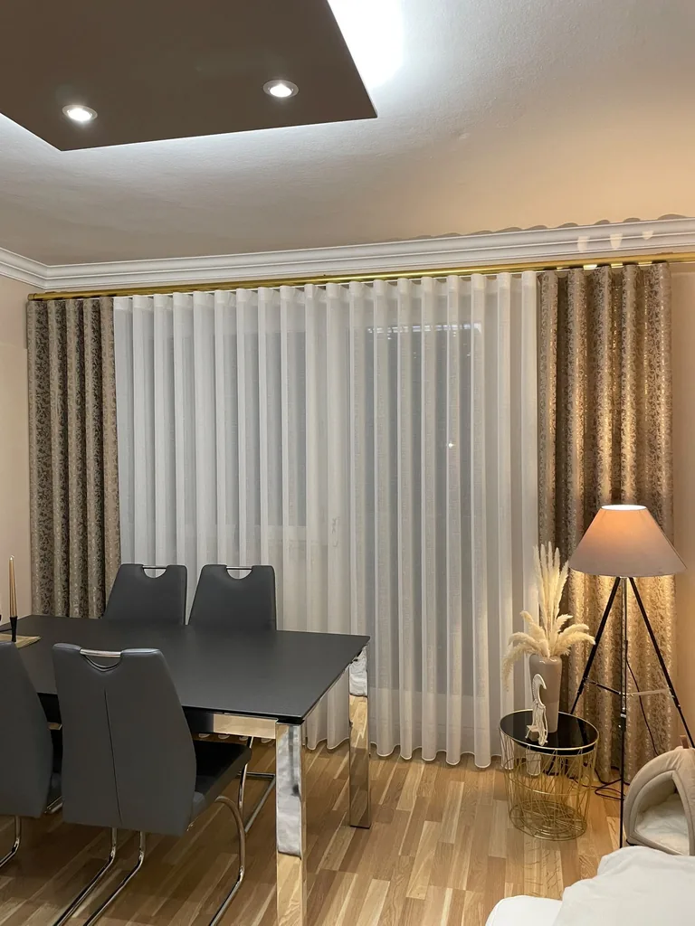 Weiße Gardinen mit goldfarben gemusterten Seitenschals an einer goldenen Gardinenstange