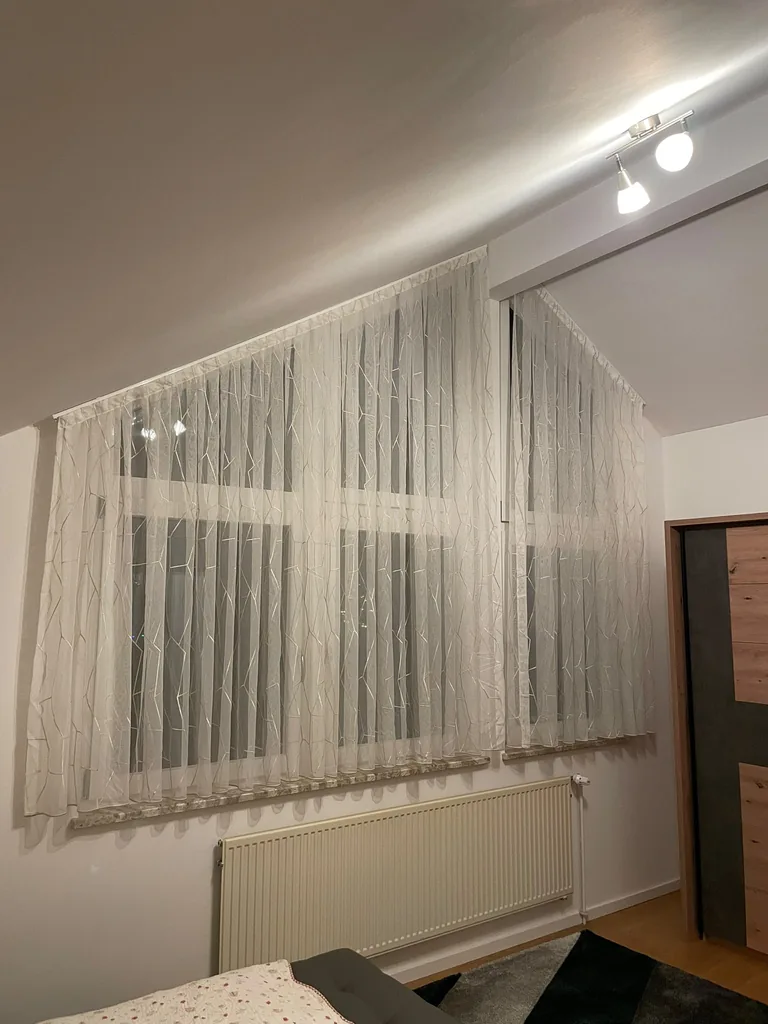 Weiße Gardinen mit Linienmuster an einem Fenster unter der Dachschräge, seitliche Ansicht