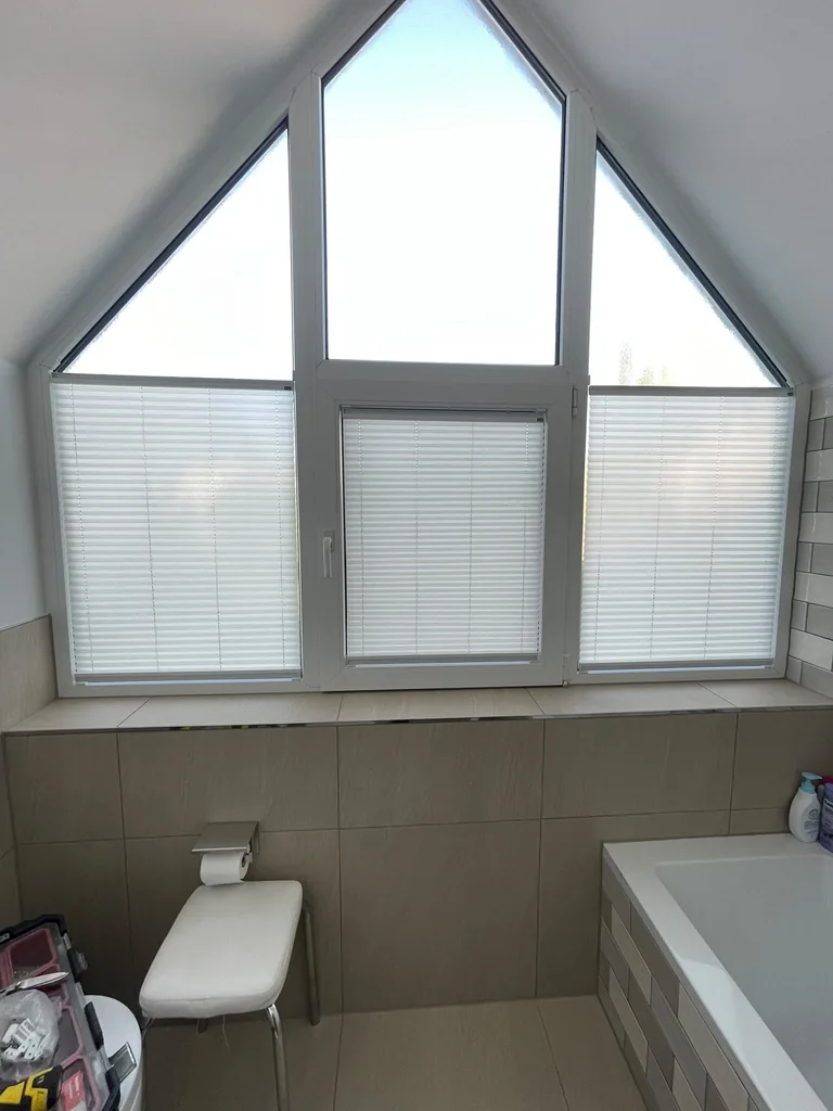 Weiße Plissees an den unteren Scheiben eines Giebelfensters im Badezimmer