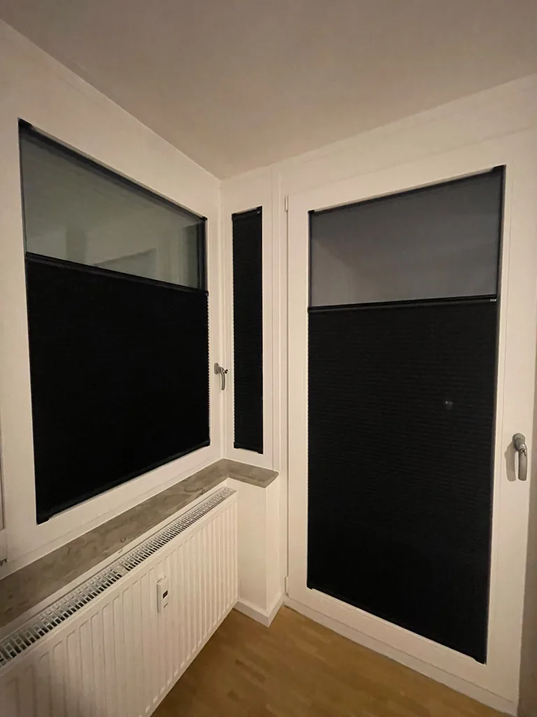 Dunkle Plissees an Eckfenster und Balkontür, im oberen Bereich teilweise geöffnet