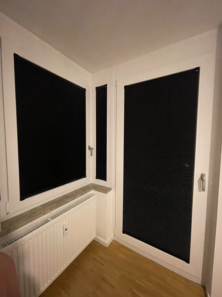 Vollständig geschlossene dunkle Plissees an Eckfenster und Balkontür